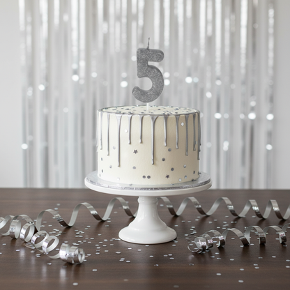 Silver glitter number 5 candle on white cake with silver drip and confetti